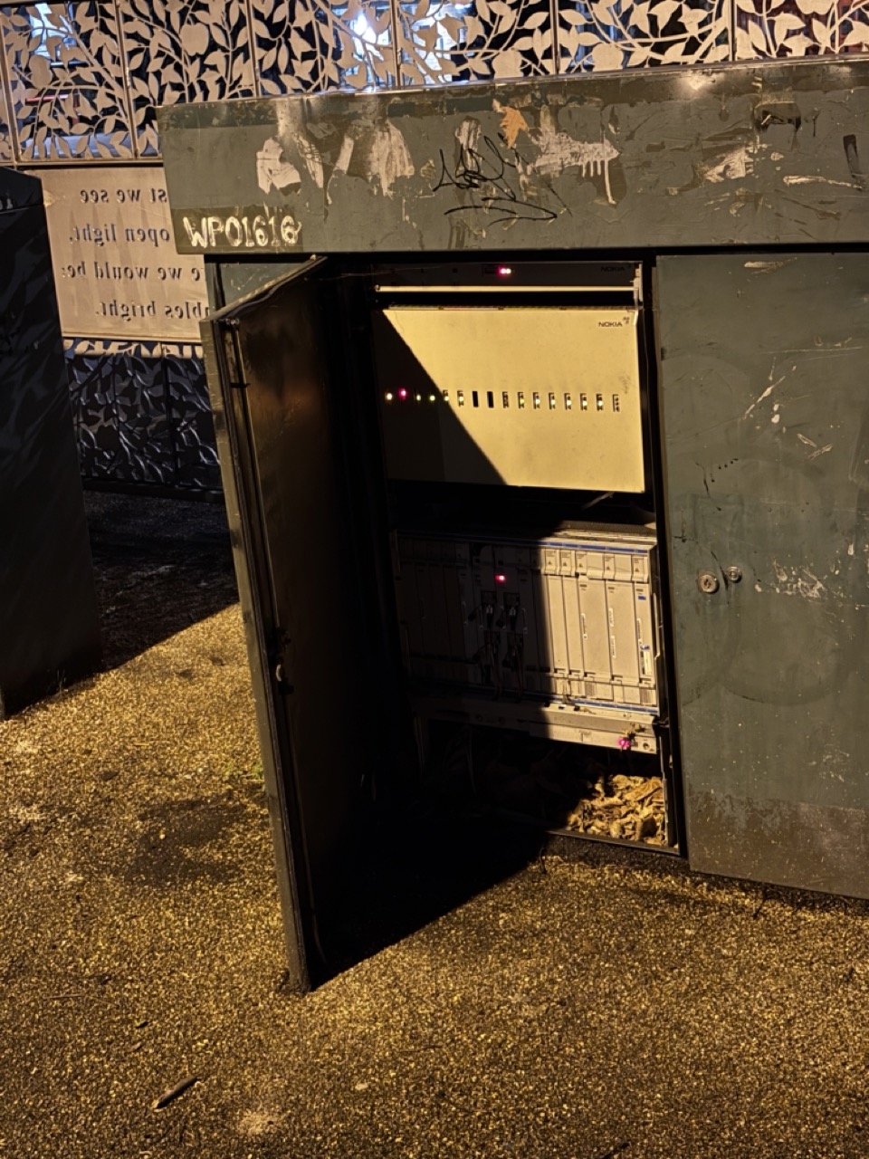 Photograph of a telecommunications street cabinet, one door is open and equipment visible and operating